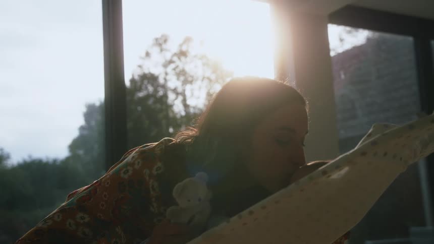 Mother kissing her baby sitting on a chair on the forehead at home