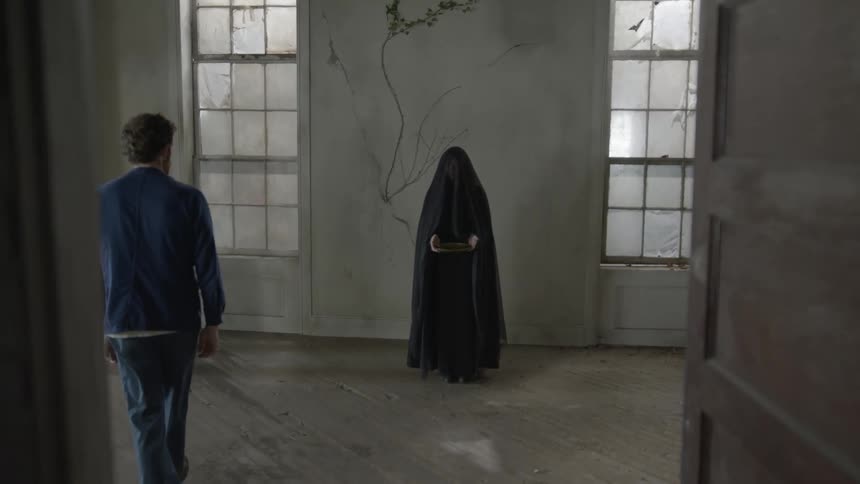 Young man enters a room where a figure covered in a black robe stands up