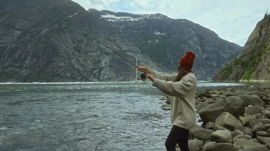 A woman stands on the shore fly fishing