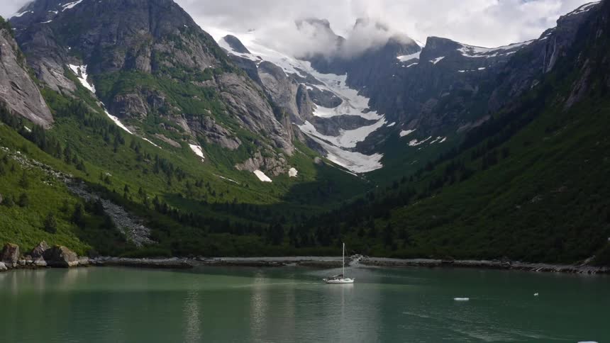 A lake with a boat with a mountain range the sky and clouds in the background
