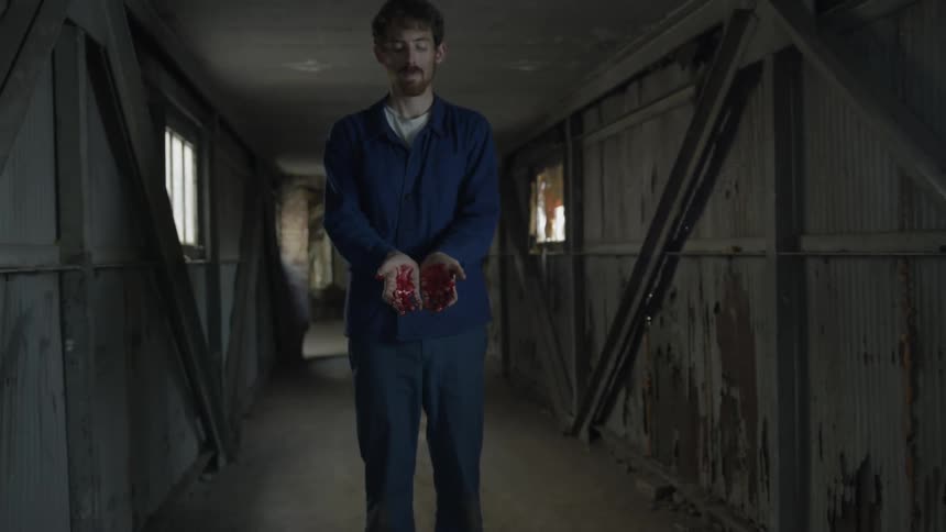 A man stands inside a building with his hands which are covered in blood held out in front of him