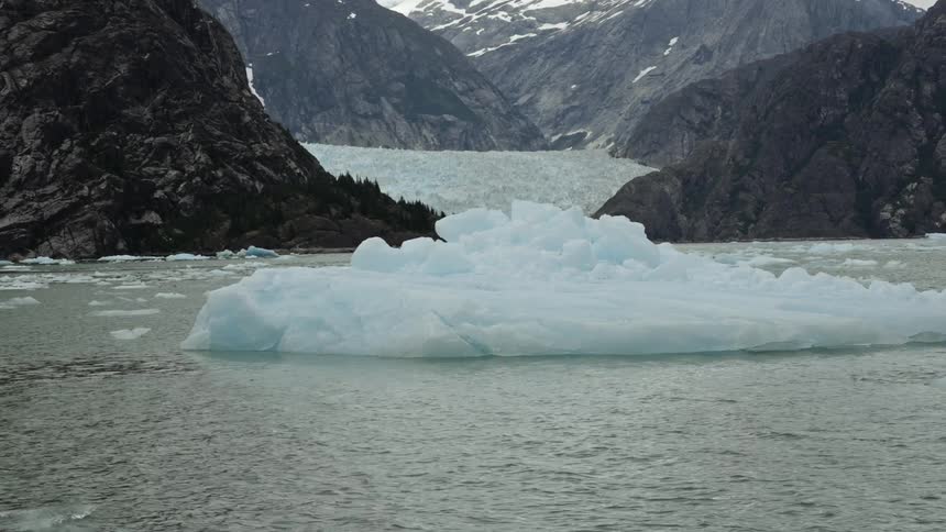 Iceberg floating in the ocean in front of a glacier in the mountains