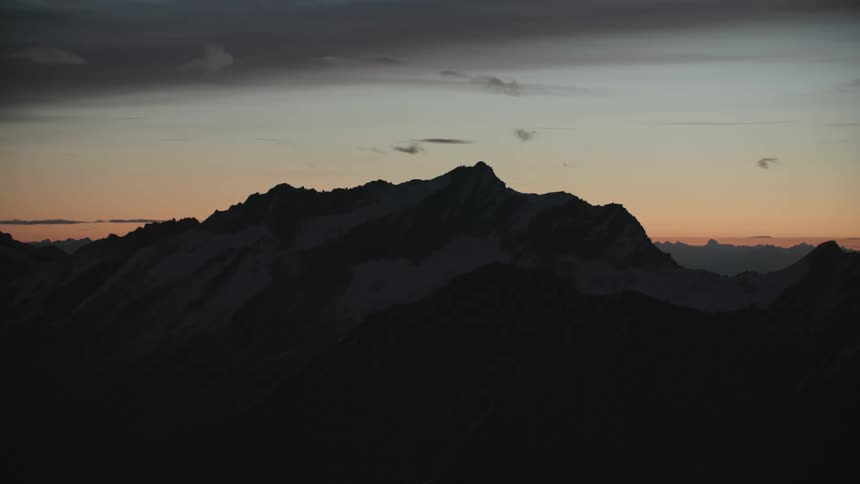 A mountain range covered in snow and ice with the sky and clouds in the background