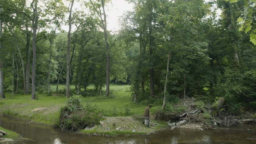 Young man carrying a metal bucket to a river near the forest