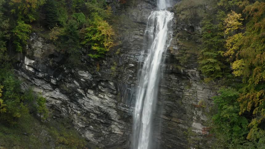 A waterfall down a tall cliff in a forest during the day