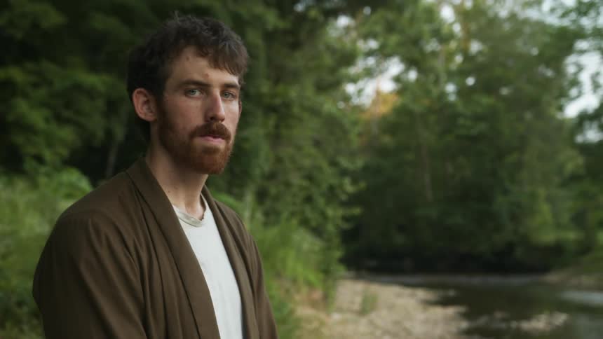 Man stands in clearing near overgrown forest