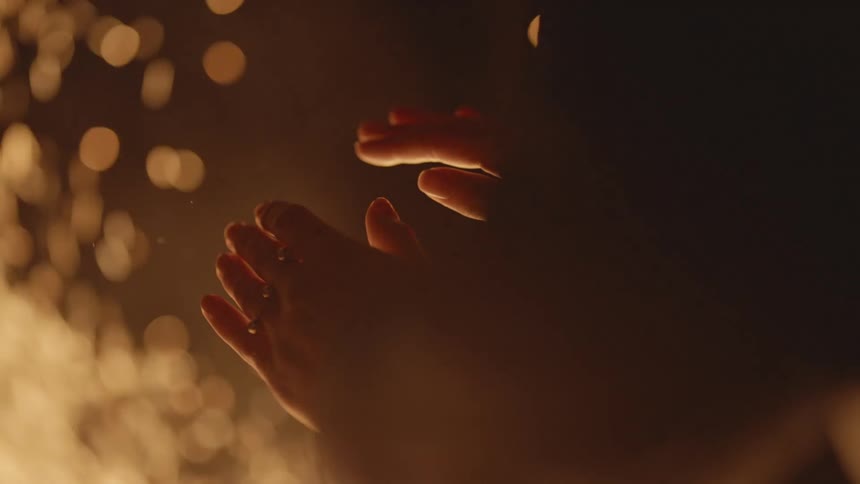 A person with rings on their fingers warming their hands in front of a fire with embers and smoke