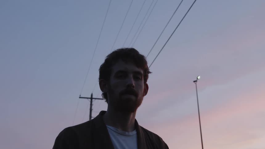 Young bearded man standing under power lines outdoors at sunset