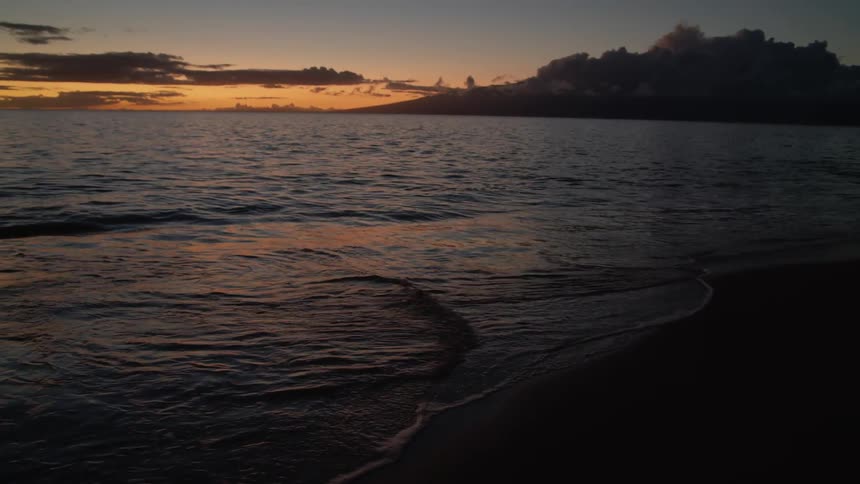 Water washes into a sandy beach at sunset