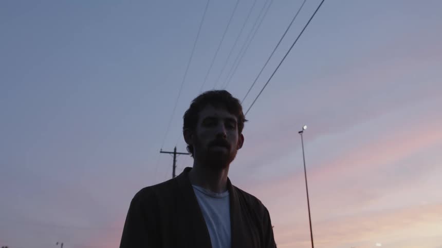 A man standing outside with a utility pole a streetlight the sky and clouds in the background