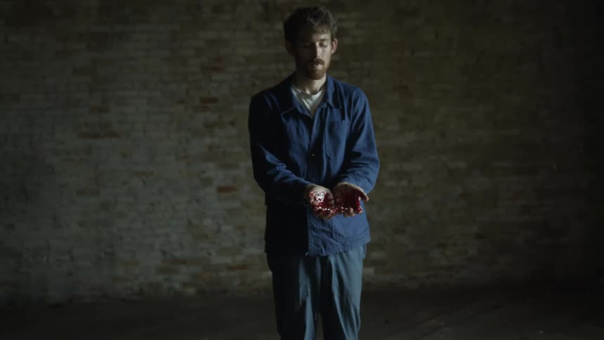 Young man stands on an empty room with his hands covered in bright red blood