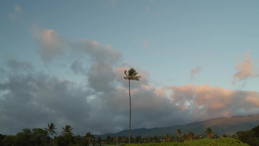 Red tinted clouds flow over palm tree dotted valley and hazy mountain