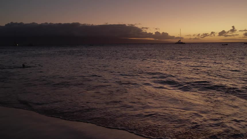 Person swimming in the sea is silhouetted against the sky at dusk seen from the beach
