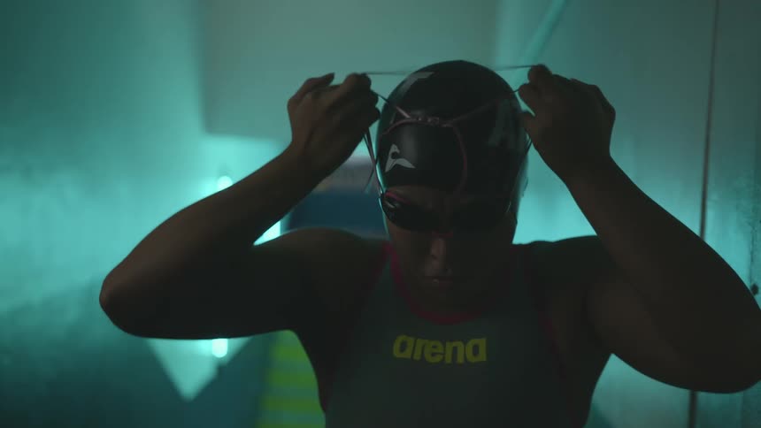 A woman with a bathing suit goggles and a swimming cap in a corridor