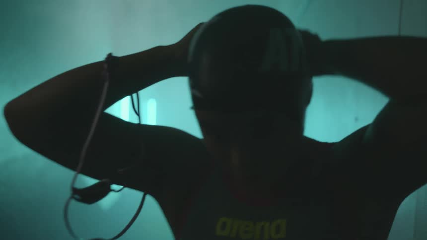 A woman with a bathing suit putting on a swimming cap in a corridor with walls