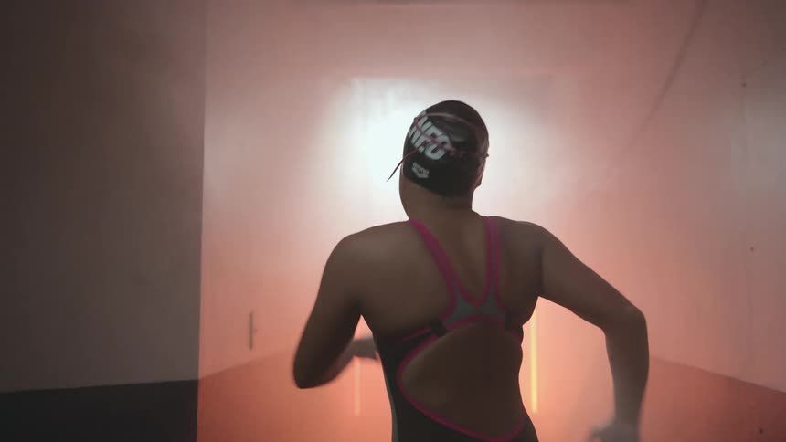 Young woman wearing swimming gear walks up and down a hallway filled with smoke and flashing orange lights