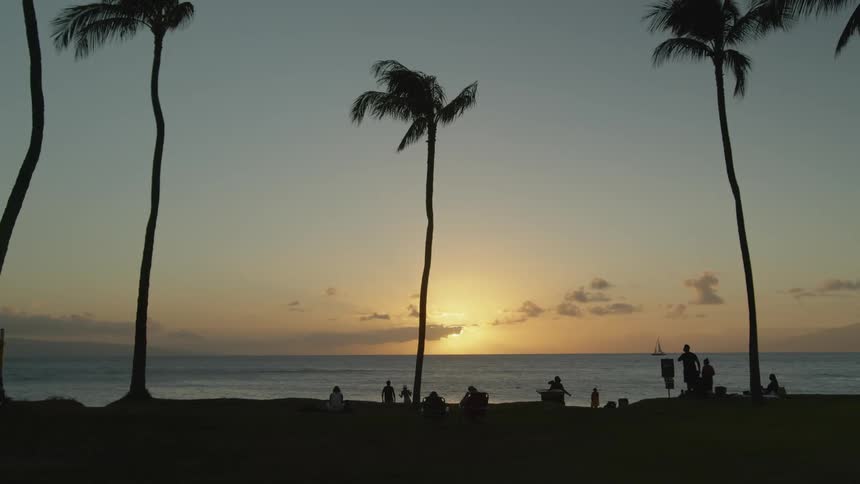 People are walking and resting on the beach at sunset