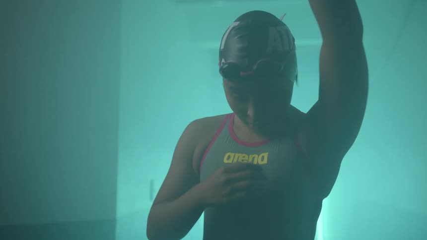A swimmer stretches her arms as she walks down the hall