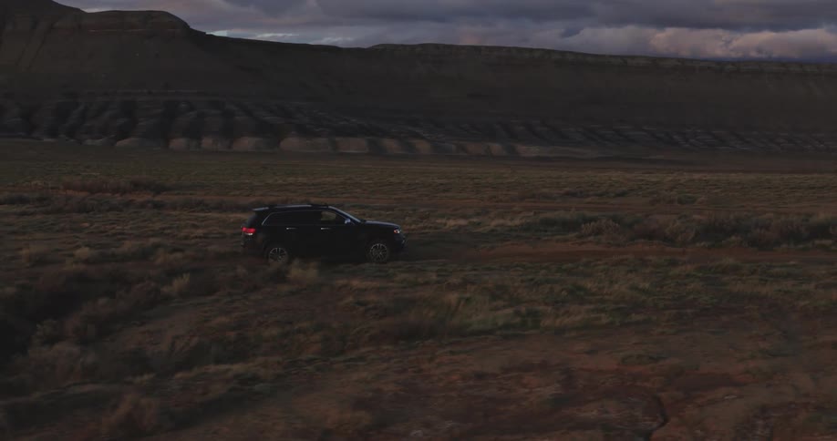 Black car driving on the badlands plains near the mountains at sunset