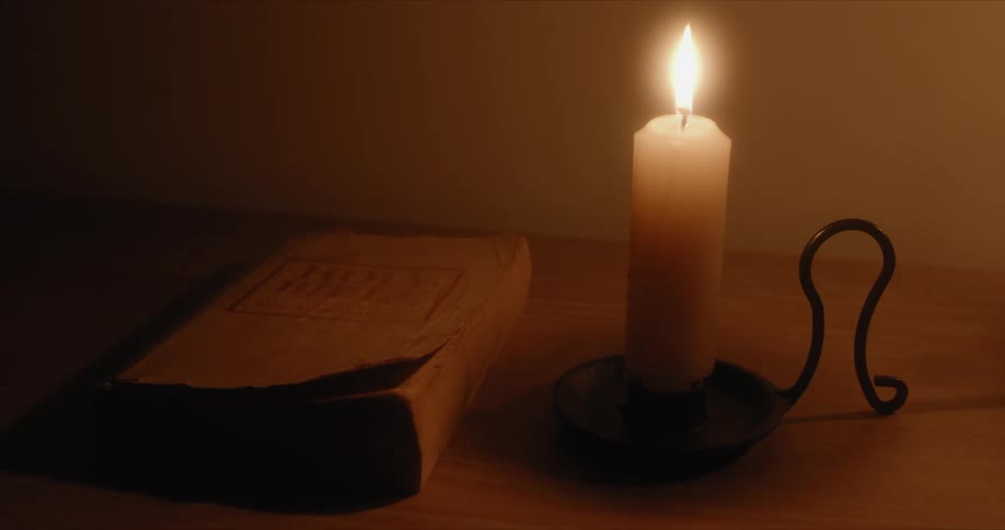 A candle is lit on a table next to a book