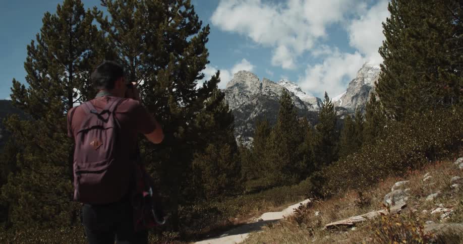 A man takes photos with his camera while hiking through the forest