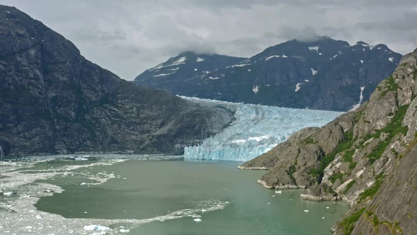 Ice floats on water near glacier and mountains on misty day