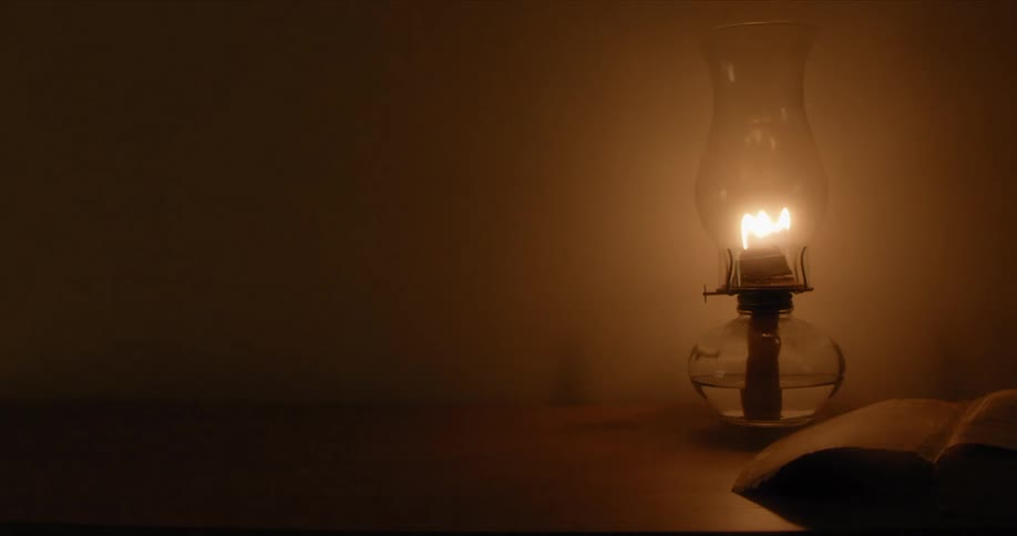 A kerosene lamp lit with fire in a room on a table with a wall in the background