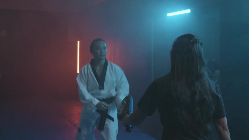 A woman practicing martial arts with a shelf trophies and a wall in the background