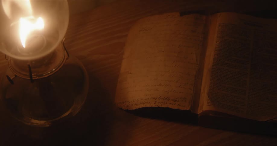 Light flickers over open book from lantern in dimly lit room