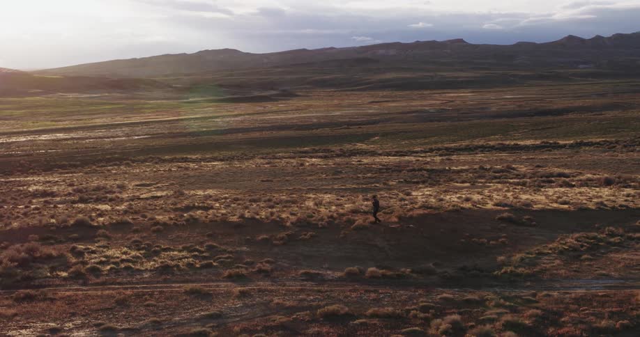 Person stands on slight incline looking across field toward mountains on sunny day