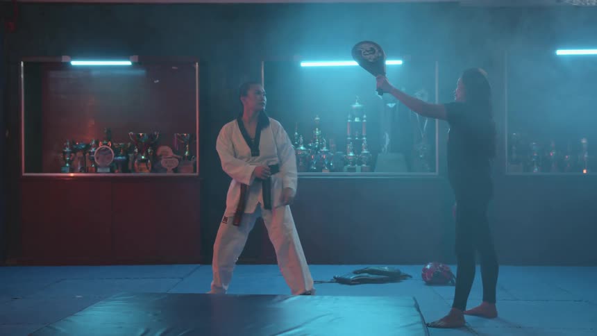 A martial artist does a high roundhouse kick to hit a kicking pad being held by a trainer