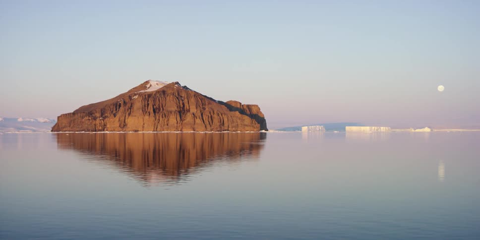 A rock formation sits in the water with ice around it