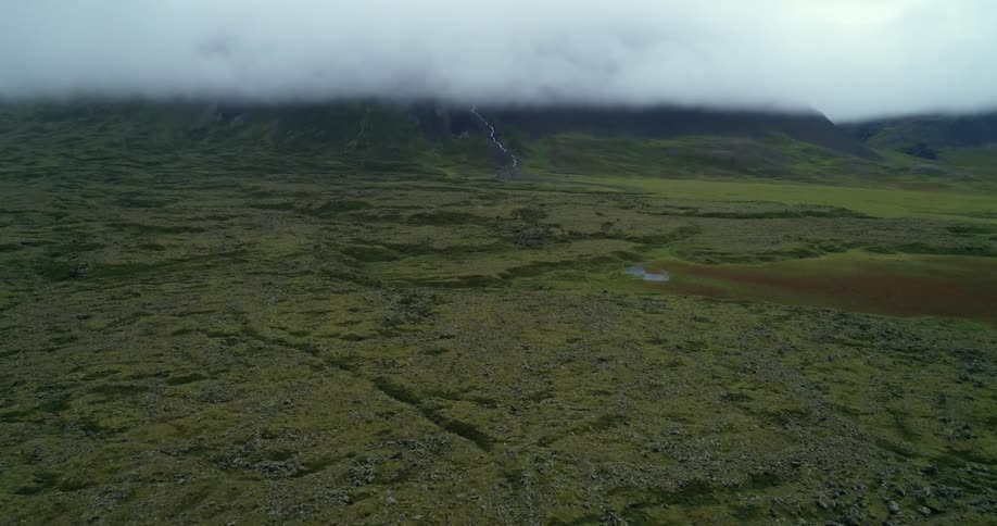Ground covered in grass and rocks and a hazy black smoke in the distance