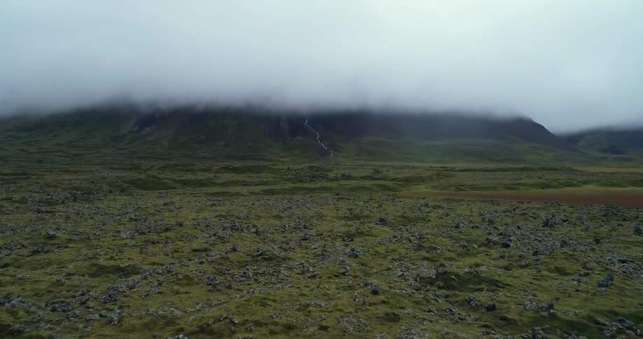 Ground covered in grass and rocks and a hazy black smoky sky in the distance