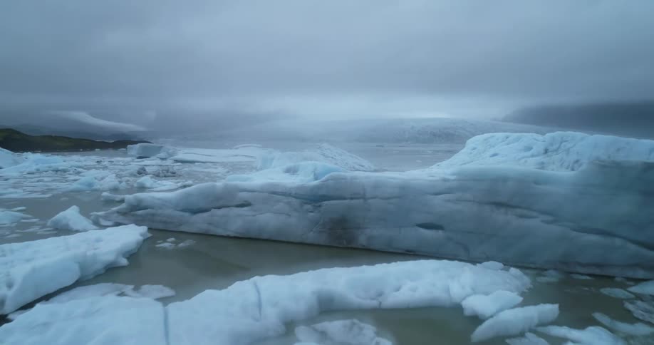 Chunks of ice broken off from glacier float on ocean water under a gray sky
