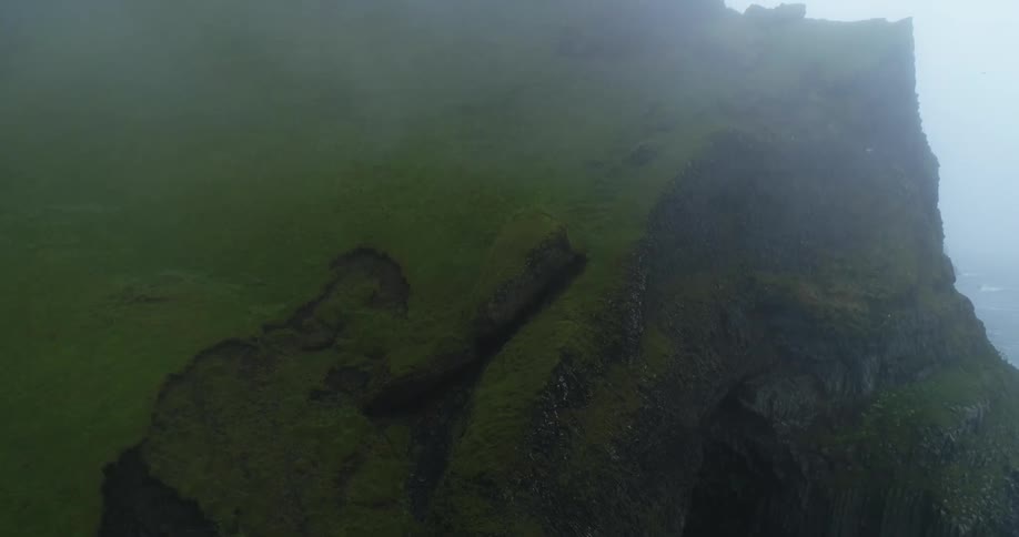 Birds are flying around the entrance to a cave in a grass covered mountain