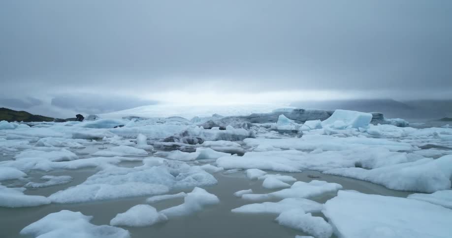 Broken up arctic ice floats on the water under a gray cloudy sky