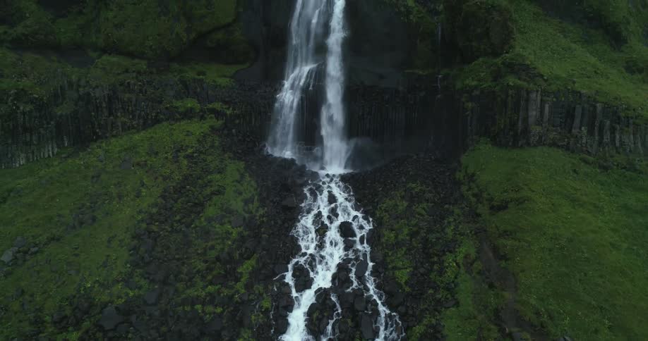 A waterfall is flowing down the side of a grassy and rocky mountain