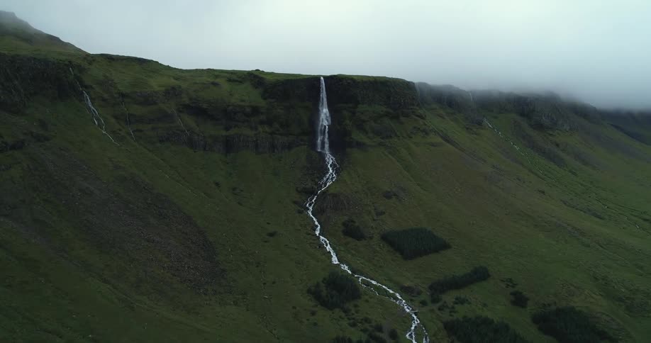 Waterfalls and a stream run down the side of a grass covered hill