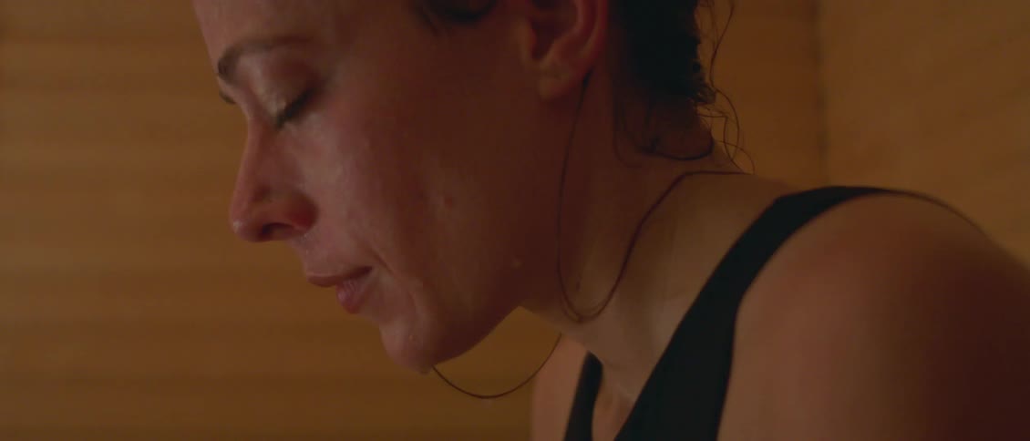 A woman sweating and relaxing in a sauna with a wall in the background