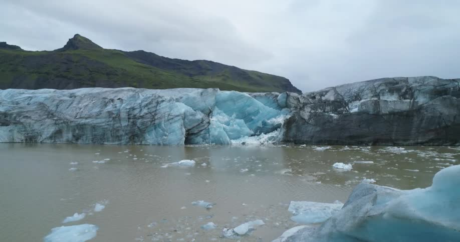 Chunks of ice are in the water and mountains are in the distance under a cloudy sky
