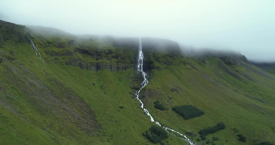 An aerial view of a waterfall and stream on mountain on a foggy day