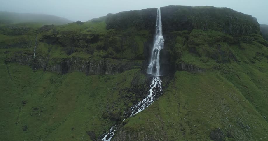 A waterfall plunges over a steep cliff in a tree covered canyon