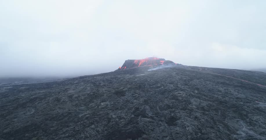 Lava erupts from the peak of a volcano on a cloudy day