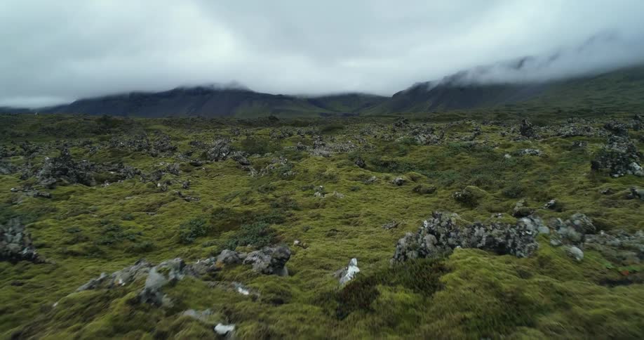 Rock outcroppings occupy vegetation covered rough terrain bordering mountains sitting under low lying clouds