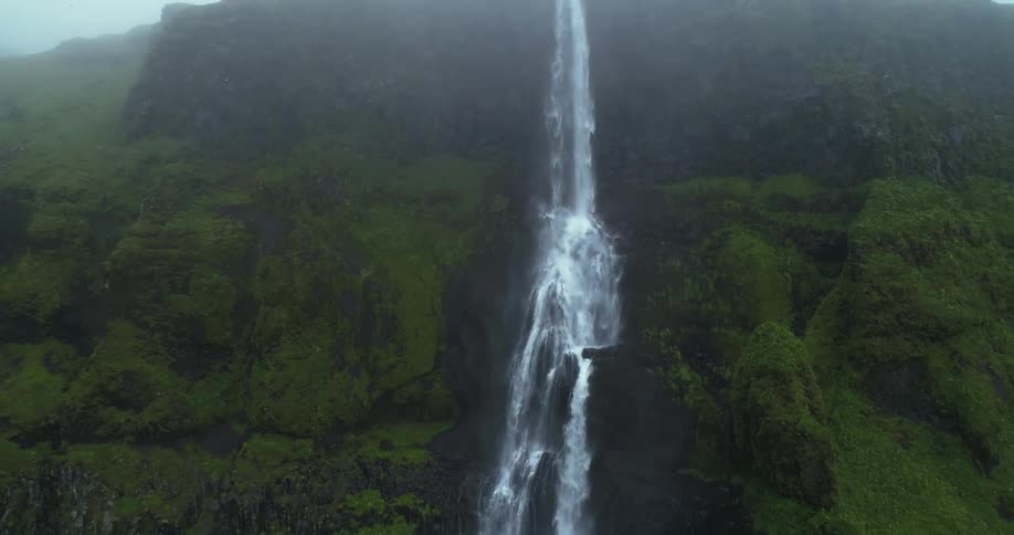 Water flows off a ridge down an almost sheer green rocky cliff
