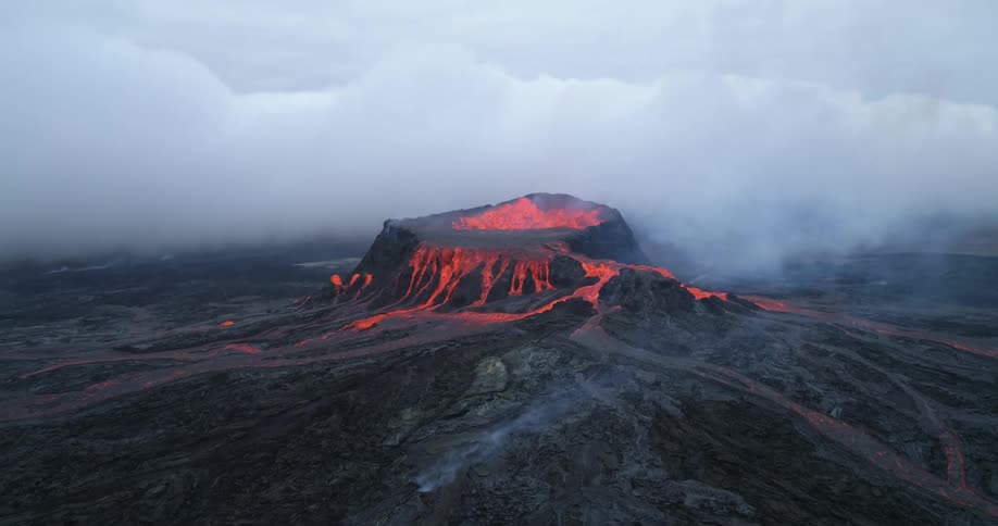 Smoke rises from bubbling lava during volcanic eruption as cloud bank flows across
