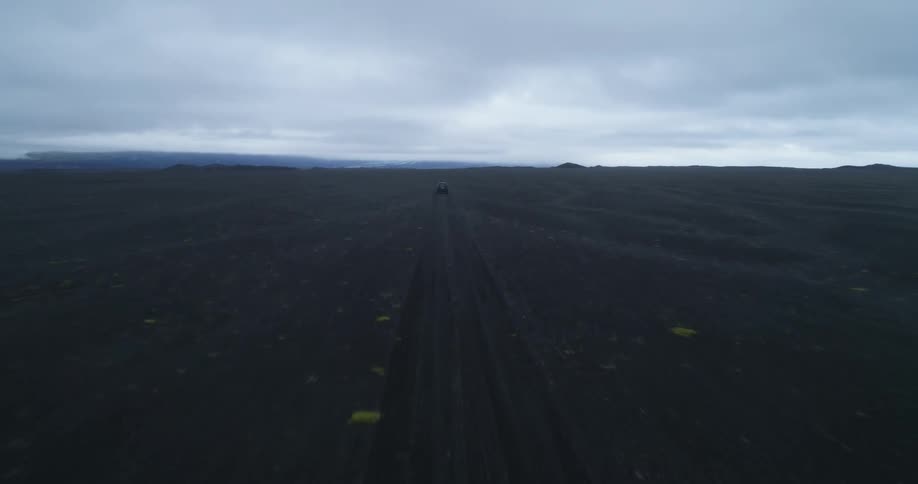 Vehicle drives down road through plain toward horizon on dim overcast day