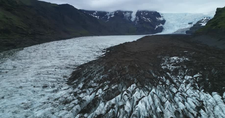 Glacier ice and snow covers ground in valley under overcast sky