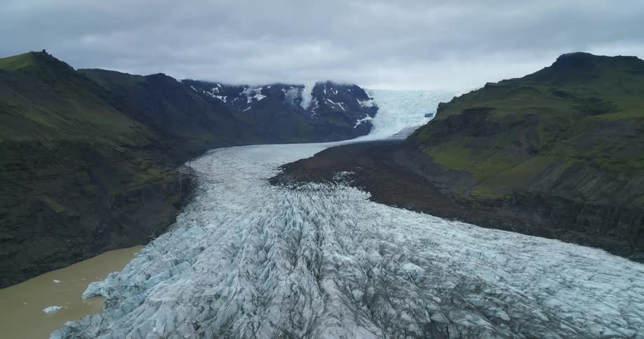 A large glacier is flowing down from mountains in the arctic wilderness